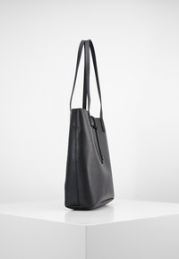Czarna skórzana torba typu tote z dwoma długimi, płaskimi paskami, pionowym zamkiem błyskawicznym oraz minimalistyczną sylwetką. Gładka faktura i usztywniony kształt.
