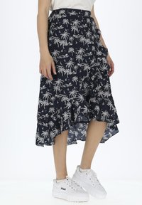 Marineblauwe rok met wit palmbomenpatroon, gerimpelde zoom en zijzakken. Gepaard met witte platform sneakers.