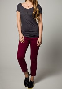 Grå kortärmad topp med rundad halsringning och knapppdetail, kombinerad med åtsittande bärnstensfärgade byxor. Svarta skor med gula sulor.