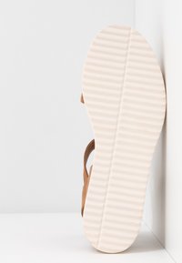 Sandale marron avec une tige texturée et une semelle en caoutchouc blanc moulé, dotée de stries horizontales pour l'adhérence et la stabilité.