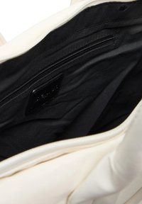 Interno di una borsa color crema che mostra la fodera in tessuto nero con tasca con cerniera e etichetta cucita all'interno.