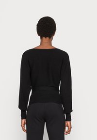 Svart stickad tröja med vid halsringning, långa ärmar, ribbad textur och åtsittande midja, matchad med svarta ribbade byxor.