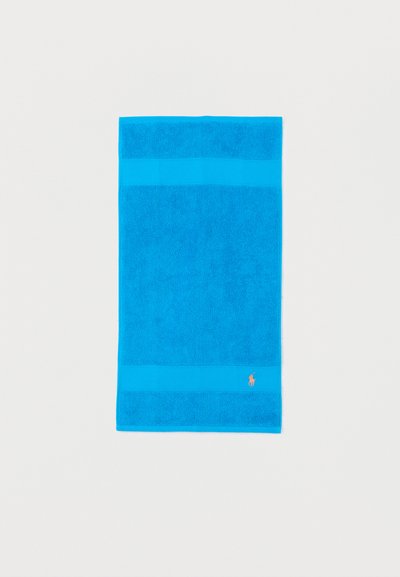 Serviette rectangulaire bleu vif avec des bandes texturées et un petit logo rose brodé près d'un coin sur fond blanc.