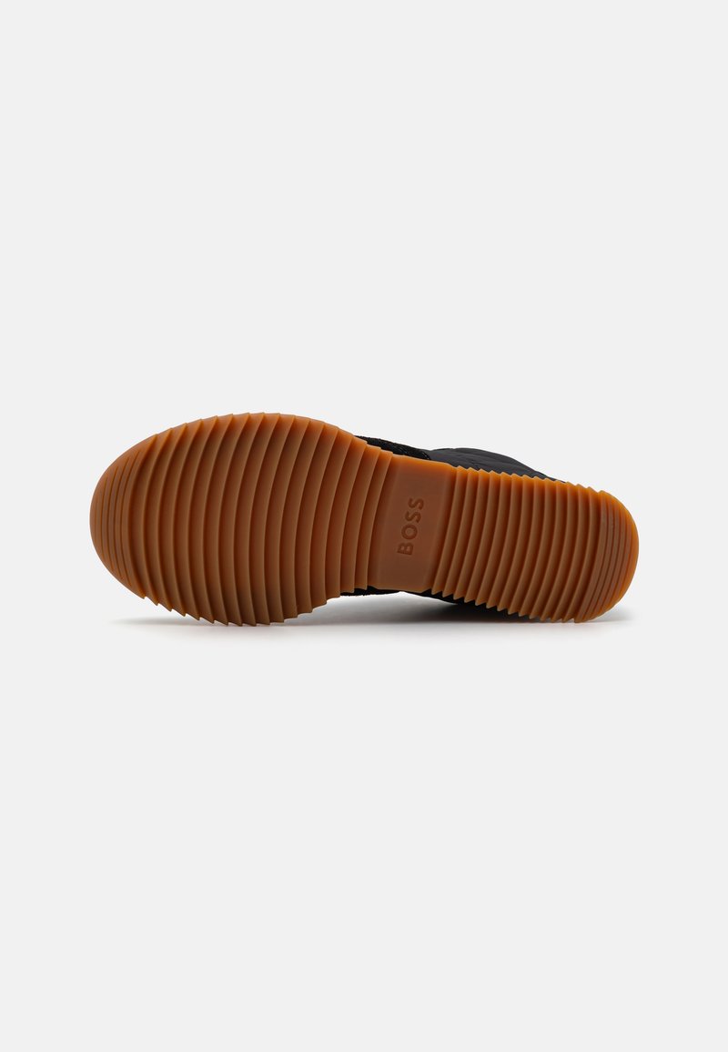 Baskets noires avec une semelle en caoutchouc texturé. La semelle extérieure présente des rainures profondes pour une adhérence optimale, et le nom de la marque "BOSS" est en relief.