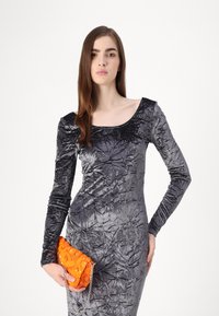 Siva haljina od crushed velveta s dugim rukavima i širokim izrezom, uparena s narančastom clutch torbicom sa šljokicama koja ima lančani remen.