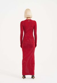 Vestido rojo de manga larga que presenta una silueta ajustada, tejido texturizado y un sutil patrón floral. La parte posterior tiene un escote redondo y un acabado suave.