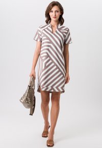 Robe à manches courtes avec un motif rayé diagonal marron et blanc, décolleté en V et fentes latérales. Modèle tenant un sac à main métallique.