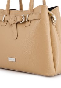 Beige leren handtas met gestructureerde vorm, dubbele handgrepen en metalen hardwareaccenten. Heeft een logoplaat aan de voorkant en een textuur op het oppervlak.