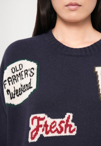 Dark navy sweater featuring knitted patches with text: "OLD FARMER'S WEEKEND" in green and white, and "Fresh" in red. Textured knit fabric.