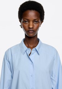 Lichtblauw button-up overhemd met een brede kraag, met subtiele stikdetails en een ontspannen silhouet. Gladde stofstructuur.