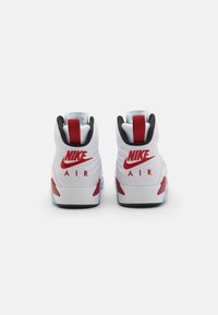 Tenisky Nike Air majú prevažne biely dizajn s červenými akcentmi, textúrovaný zvršok a čierny golier. Logo je výrazne zobrazené.