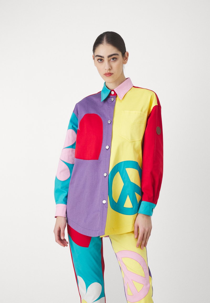 Multicolored oversized shirt with purple, yellow, red, and turquoise panels; features geometric shapes and a chest pocket; button-up design.