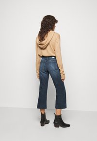 Sudadera beige con capucha combinada con pantalones cortos de mezclilla azul oscuro y botas de tobillo negras. Tejido texturizado y diseño de corte relajado.