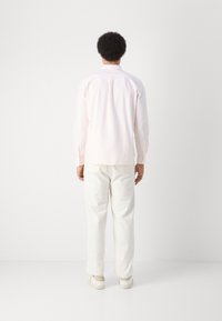 Camicia rosa chiaro con bottoni, pantaloni bianchi e sneakers beige. La camicia presenta un colletto e maniche lunghe, con una linea dritta.