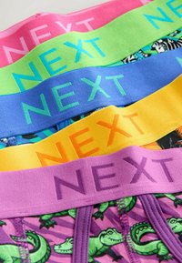 Négy pár színes alsónemű különböző mintákkal. Az elasztikus derékszíjak pink, zöld, kék, sárga és lila színűek, és a "NEXT" márkajelet viselik.