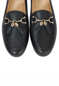 Black leather loafers featuring a gold hardware accent with a double strap and two dark blue tassels at the front. Smooth texture.