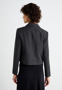 Lyhennetty harmaa pinstripe-bleiseri, jossa on viisitaskullinen kaulus, napilliset hihansuut ja sileä pinta, suunniteltu istuvaksi takana.