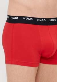 Röda kalsonger i boxerstil gjorda av en mjuk bomullsblandning, med ett svart elastiskt midjeband som har den upprepade "HUGO"-loggan i vitt.