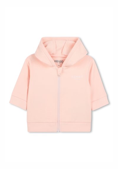 Hoodie zippé rose clair en tissu doux, avec un petit logo blanc sur la poitrine et des manches courtes, doté d'une capuche et de poignets côtelés.