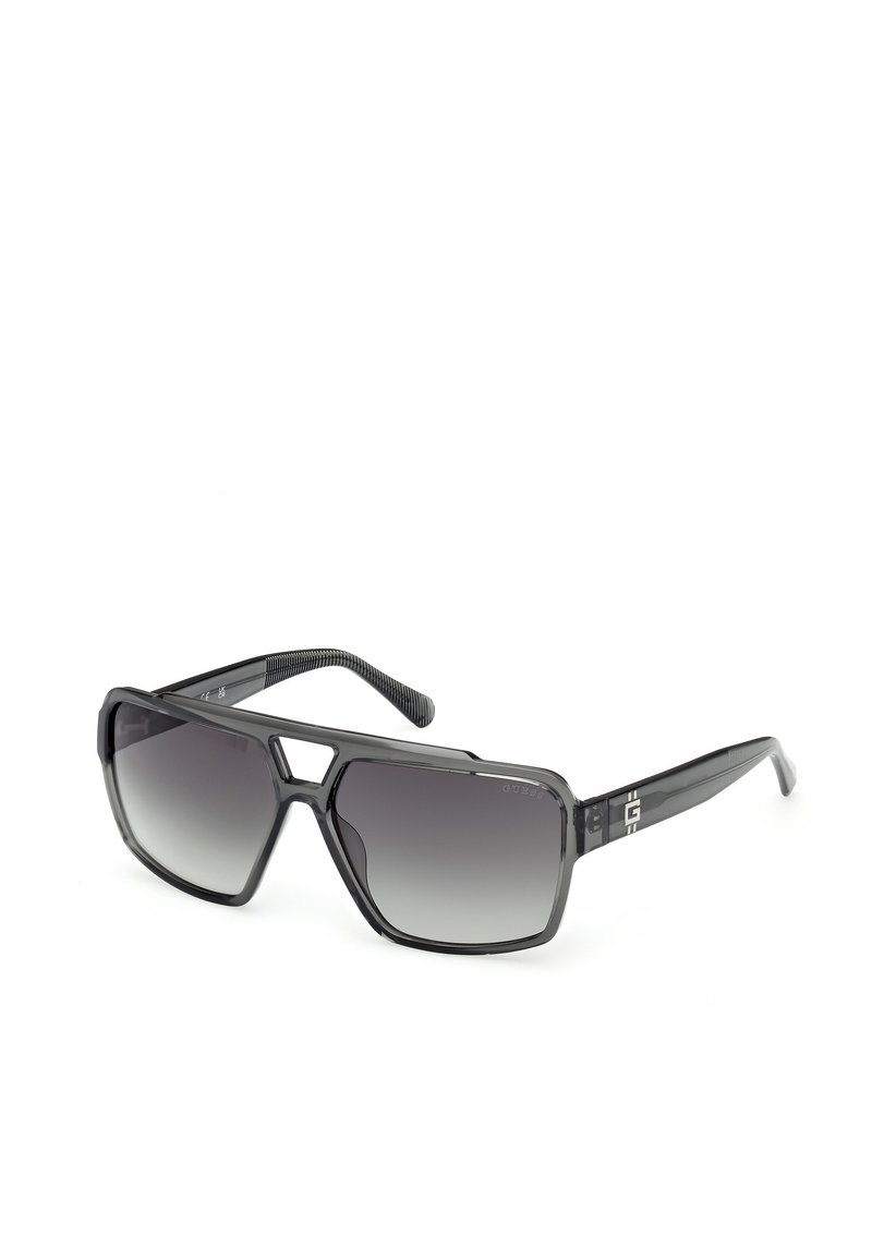 Gafas de sol con un gran marco de plástico negro angular, lentes gris degradado y brazos negros texturizados con detalles del logotipo.