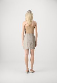 Beige tetts tanktop og lys grå miniskjørt. Skjørtet har glidelås bak og er laget av glatt stoff. Sandaler med tynne høye hæler.