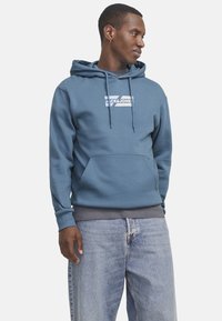 Blue cotton hoodie with a kangaroo pocket, drawstring hood, and white logo print. Features ribbed cuffs and a relaxed fit.