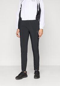 Juodi sportiniai kelnių, pritaikyti prisitaikančiam siluetui, pagaminti iš lengvos medžiagos, su elastingu juosmeniu ir nežymiu logotipo detaliu ant šlaunies.