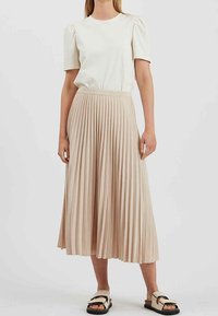 Beige geplooide rok met een aansluitende tailleband, gecombineerd met een kortemouwen, crèmekleurig top van lichtgewicht stof. Sandalen met een ontwerp met banden.