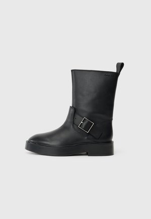 Black leather ankle boot with a rounded toe, flat sole, and a silver buckle accent on the side. Features a pull tab at the back.