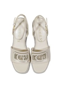 Sandali slingback beige con tomaia in vernice lucida, accenti in hardware dorato e dettagli del logo sulle cinghie. Soletta leggermente imbottita.