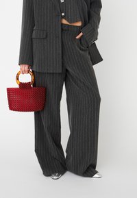 Costume gris à rayures fines avec une coupe décontractée, associé à un sac à main en perles rouges doté d'une anse en plastique orange et de chaussures argentées à bout pointu.