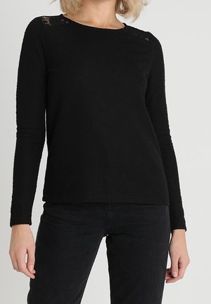 Haut noir à manches longues en tissu texturé avec un col rond et de subtils accents en dentelle aux épaules. Ajustement ajusté.