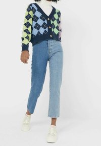 Háčkovaný cardigan v námořnické modři s barevným argyle vzorem, s výstřihem do V a čtyřmi dřevěnými knoflíky. V kombinaci se světle modrými džíny rovného střihu a bílými teniskami.