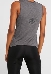 Šedé sportovní tílko bez rukávů s kulatým lemem a logem Reebok CrossFit Games 2019 na zádech. Měkký materiál a volný střih.