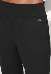 Czarne spodnie treningowe z szerokim paskiem, z dwoma bocznymi kieszeniami i subtelnymi detalami przeszyć. Miękki, elastyczny materiał.