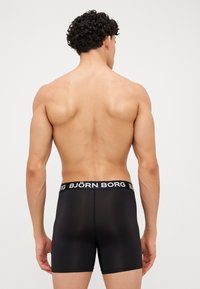 Schwarze Boxershorts mit einem weißen elastischen Bund mit "BJÖRN BORG"-Logo. Der Stoff wirkt glatt und leicht transparent und schmiegt sich eng an.