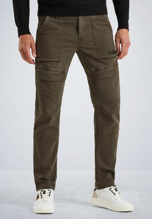 Pantalons cargo en tissu vert olive avec plusieurs poches sur le devant et des coutures renforcées. Associés à des baskets blanches avec des accents noirs.