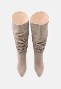 Gurķu auguma taupe krāsas zamša zābaki ar rūpīgi sarullētu dizainu, smailu purngalu un gludu iekšpusi. Ar platu zoli, minimālu apdari un diskrētu tekstūru.