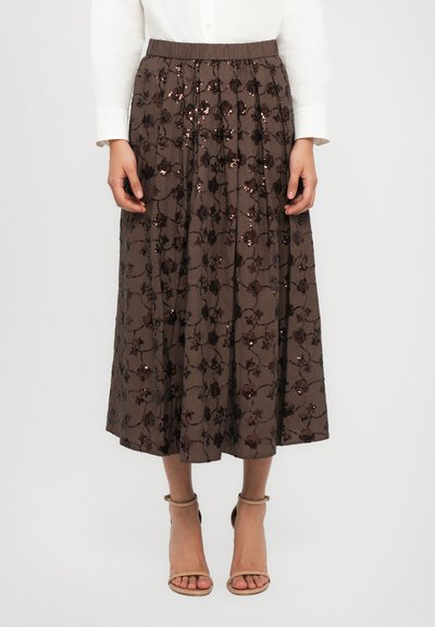 Jupe plissée marron avec un motif floral et des sequins, dotée d'une taille élastique. Portée avec des sandales à brides beiges et un haut blanc.