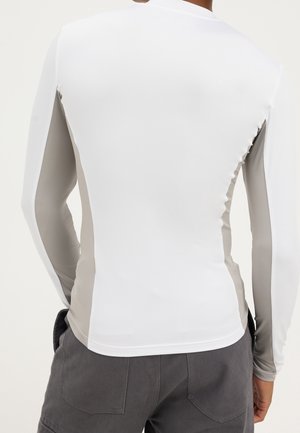 Chemise à manches longues ajustée avec un devant blanc et des panneaux latéraux gris portée par une personne de dos, associée à un pantalon gris foncé.