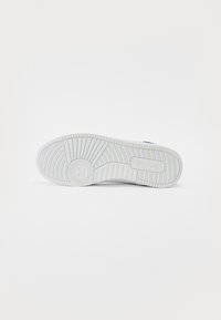 White sneaker outsole with textured rubber; features horizontal and vertical grooves, a circular pivot design in the center, and branding.