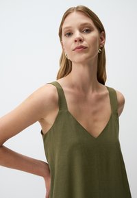 Abito senza maniche verde oliva con scollatura a V, realizzato in un tessuto testurizzato. Presenta spalline larghe e una vestibilità morbida.