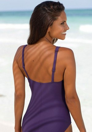 Lila Einteiler-Badeanzug mit dünnen, verstellbaren Trägern, glatter Textur und schlichem Design, von hinten am Strand betrachtet.