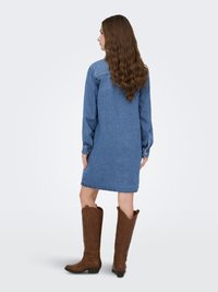Denim dress with long sleeves, a button-down front, and a slightly loose fit, paired with brown leather cowboy boots featuring a textured pattern.