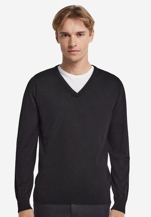 Schwarzer V-Ausschnitt-Pullover, lange Ärmel, schlanker Schnitt. Hergestellt aus weichem Stoff mit geripptem Besatz am Kragen und an den Ärmelbündchen. Getragen über einem weißen T-Shirt.