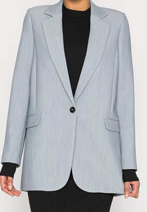 Lysegrå blazer med enkelt knap og åbne revers båret over en sort langærmet top og en sort ribbet nederdel.
