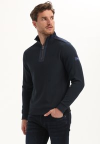 Tume sinine pullover, mis on valmistatud tekstuuriga kangast, millel on veerandi tõmbamisega krae, kontrastsete õlavarre aktsentide ja ribakujuliste varrukatega.