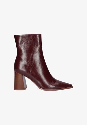 Botín de cuero burdeos con punta afilada, tacón alto en bloque y un acabado brillante. Presenta una textura suave y una silueta elegante.
