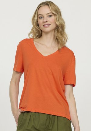 T-shirt orange à col en V en tissu doux, doté de manches courtes et d'une coupe décontractée. Le design présente des lignes épurées sans motifs ni accents visibles.