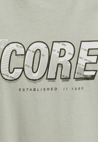 KERN-Text mit Binärcode und Linienmuster in Blockbuchstaben, darüber "ETABLIERT // 1990" auf lichtfarbener Stoffoberfläche.